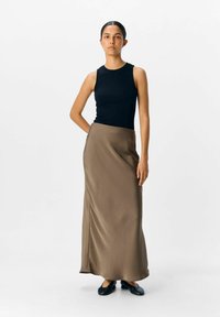 Top in cotone nero a costine e gonna maxi in satin khaki con caduta fluida. L'outfit è abbinato a scarpe basse nere, esposto su uno sfondo chiaro.