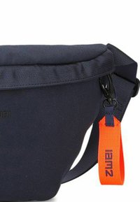 Borsa a tracolla in tessuto navy con parte superiore imbottita, tracolla regolabile, hardware acrilico e un'etichetta arancione in contrasto. Presenta un design minimalista.