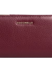 Portafoglio in pelle bordeaux con finitura textured, caratterizzato dal logo dorato "Coccinelle" sulla parte anteriore. Forma rettangolare compatta.