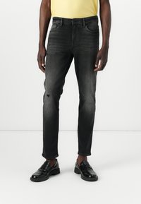 Jeans negri din denim cu o croială slim, prezentând decolorări subtile și o genunchiere uzată. Finisaj clasic cu cinci buzunare și talie cu bucle pentru curea.