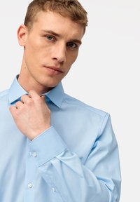Camicia azzurra chiara, in cotone, colletto a punta, maniche lunghe, polsini con un bottone, texture liscia, vestibilità ben sagomata.