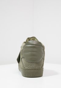 Zapatilla alta verde de ante con un panel de cuero texturizado, perforaciones en los laterales y un cuello acolchado para mayor soporte.