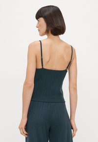 Débardeur en rib avec une couleur bleu sarcelle foncé, doté de fines bretelles réglables, d'un design ajusté et d'un ourlet droit, mettant en avant un tissu simple et texturé.