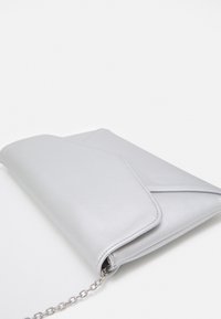 Clutch de cuero plateado con solapa triangular, cadena como correa y textura lisa. Presenta líneas limpias y un diseño minimalista.