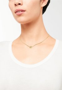 Guld kæde med en geometrisk hjertependant. Kæden er tynd med en glat tekstur, der komplementerer det minimalistiske design.