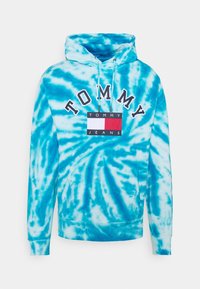 Huvtröja i blått tie-dye-mönster, med en logotyp framtill med texten "TOMMY" och en rektangulär design i röd, vit och blå.