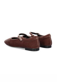 Zapatos Mary Jane de terciopelo marrón con punta afilada, que presentan una correa en el empeine y un tacón bajo de goma negra. Textura suave y detalles mínimos.