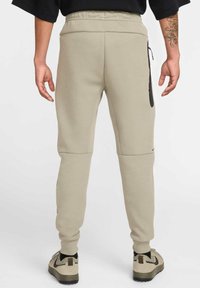 Helle beige Sweatpants mit einem elastischen Bund, seitlichem Reißverschluss-Taschen und gerippten Bündchen. Kombiniert mit passenden beigen Sneakers.