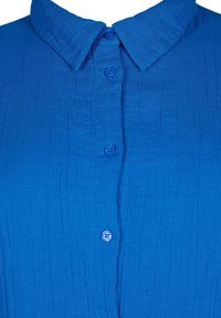 Blue collared shirt made of textured fabric, featuring six buttons down the front and a crinkled appearance, enhancing its visual depth.