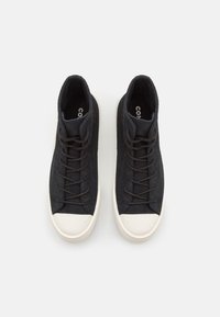 High-top black canvas sneakers featuring a white rubber toe cap, round laces, and a textured finish. Logo inside the shoe visible.