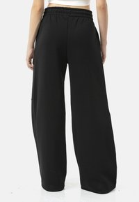 Zwarte broek met wijde pijpen en een elastische tailleband, gemaakt van een zachte stof met een gladde textuur zonder zichtbare patronen of accenten.