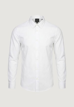 Biała koszula na długi rękaw z kołnierzykiem w szpic, zapinana na guziki z przodu, z metką projektanta wewnątrz kołnierza.