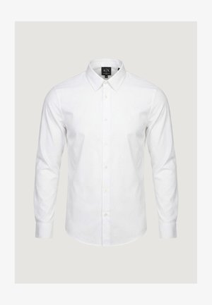 Biała koszula na długi rękaw z kołnierzykiem w szpic, zapinana na guziki z przodu, z metką projektanta wewnątrz kołnierza.