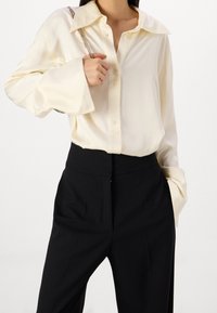 Krémová košile na knoflíky s velkým límcem, měkkou texturou a širokými rukávy, spárovaná s černými kalhotami s vysokým pasem.