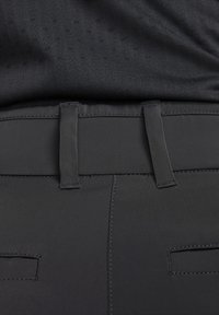 Los pantalones deportivos negros presentan una textura suave con costuras planas, una cinturilla ancha y dos bolsillos traseros con suturas horizontales sutiles.