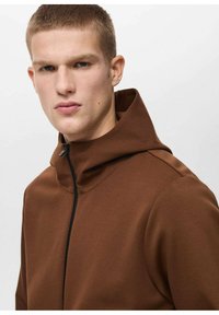 Giacca cappuccio marrone con colletto alto, dotata di una zip nera. Tessuto liscio e testurizzato con un design aderente.