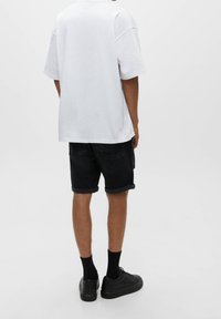 Biała, oversize t-shirt w połączeniu z ciemnoniebieskimi szortami dżinsowymi, podwiniętymi u dołu. Czarna para sneakersów i skarpetki dopełniają wygląd.