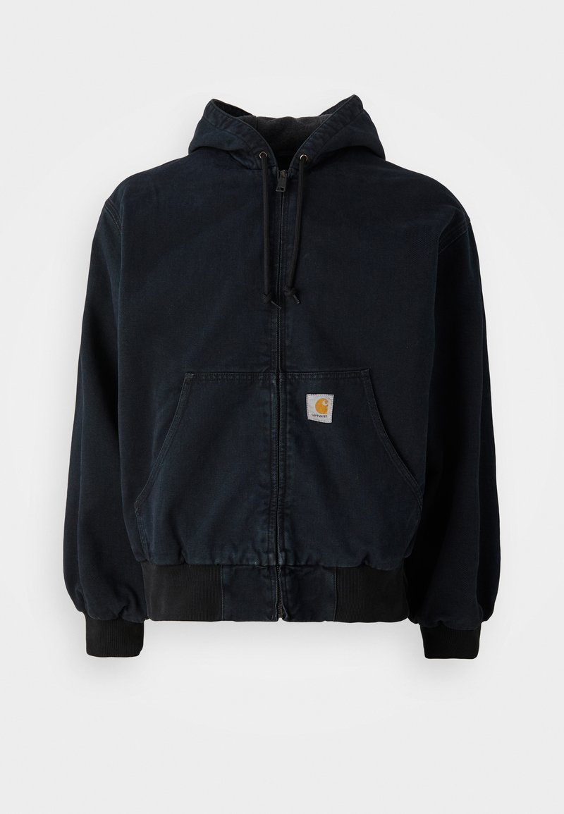 Schwarze Zip-Hoodie mit Fronttaschen, Kordelzugkapuze, gerippten Bündchen und Saum, mit einem kleinen rechteckigen gelben Logo-Patch auf der Tasche.