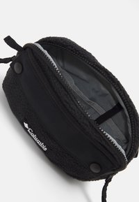 Saco de pelúcia preta com fecho de zíper, forro cinza liso e uma alça lateral. Marca Columbia visível na parte da frente.