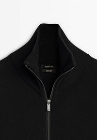 Maglione nero con zip, caratterizzato da un colletto alto e una zip in argento. Il tessuto presenta un motivo testurizzato con un rivestimento interno liscio.