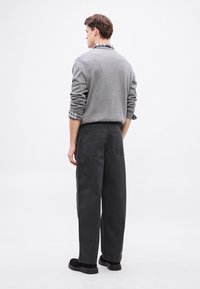 Szürke pulóver, kerek nyakkal és mandzsettás ujjakkal, sötét, laza szabású nadrággal és fekete cipővel párosítva. Egyszerű, tiszta dizájn.