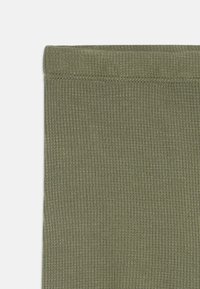 Primo piano di un tessuto a maglia a coste verde oliva con una vita cucita su sfondo bianco.