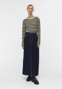 Haut à rayures à manches longues en crème et noir, associé à une jupe maxi en denim foncé avec une couture frontale et deux poches latérales. Bottines noires.