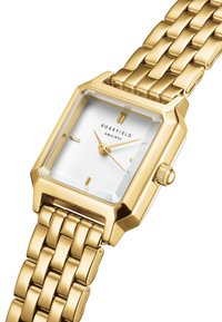 Montre carrée dorée avec un cadran blanc, verre surélevé et bracelet en métal maillé. Présente une couronne et des marqueurs horaires minimalistes.