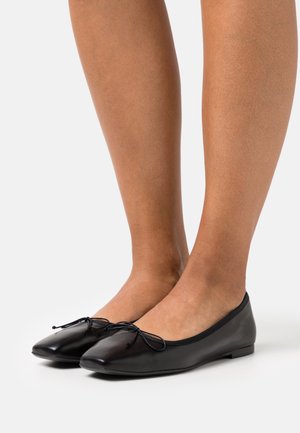 Ballerines en cuir noir avec un bout pointu, ornées d'un nœud décoratif à l'avant et d'une semelle plate. Texture lisse et design élégant.
