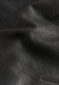 Țesătură din piele texturată neagră cu o suprafață acoperită de bolovani, având pliuri moi și o strălucire subtilă, cusută de-a lungul marginii.