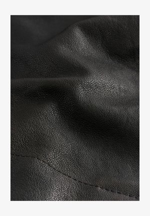 Czarna skórzana tkanina teksturowana z powierzchnią o fakturze drobnych kamieni, prezentująca miękkie fałdy i subtelny połysk, zszyta wzdłuż krawędzi.