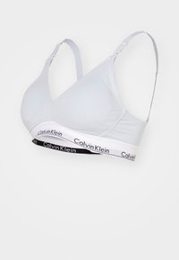 Gaišpelēks mīksts krūšturis ar regulējamām siksnām un plašu elastīgu lentu, kurai ir kontrastējošs melnbalts Calvin Klein logotips.