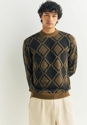 Knit sweater featuring a textured diamond pattern in brown and navy with a ribbed crew neckline and hem. Worn over light-colored trousers.