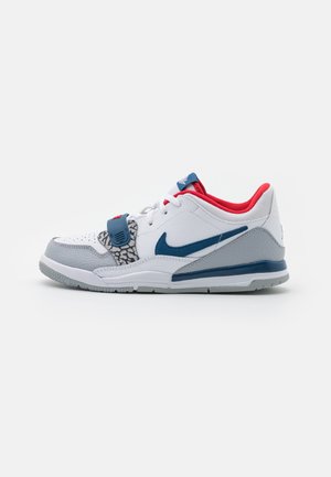 White sneaker with gray accents, featuring a textured gray overlay, blue swoosh, and red collar. Includes patterned detail on the tongue.