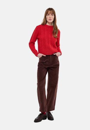 Pull rouge en maille torsadée avec un col rond, associé à un pantalon large en velours côtelé marron et des chaussures noires à lacets.