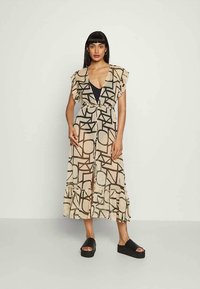 Vestido beige con patrones geométricos negros, mangas acampanadas y dobladillo con volantes. Combinado con sandalias de plataforma negras, con un diseño de escote en V profundo.