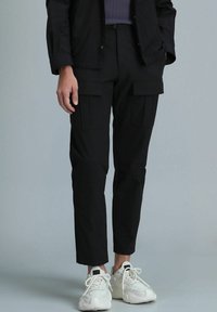 Zwarte cargobroek met een tapered fit, twee voorzakken en een subtiele textuur. Gecombineerd met witte sneakers, die veters en een minimalistisch ontwerp tonen.