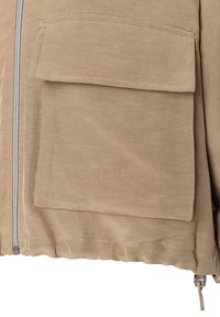 Beige Jacke aus strukturiertem Material, mit durchgehendem Reißverschluss und einer großen vorderen Tasche mit Klappe. Der Saum ist mit Gummizug gerafft.
