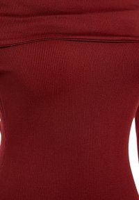 Gros plan sur un tissu côtelé rouge foncé avec un détail de couture horizontale près du haut, montrant la texture et l’élasticité d’un vêtement.