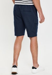 Marine cargo shorts lavet af bomuld med elastisk talje, sidelommer til cargo og to baglommer. Båret med hvide sneakers.