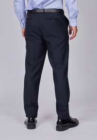 Pantalons habillés bleu marine à la coupe épurée, dotés de deux poches arrière et d'une texture lisse, associés à des chaussures de ville noires.