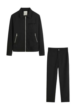 Veste noire avec fermeture éclair frontale et poches zippées, associée à un pantalon noir assorti avec fermeture par bouton.