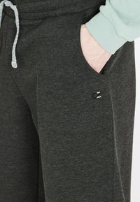 Donkergrijze sweatpants met een zachte textuur, voorzien van een elastische tailleband, trekkoord, zijzakken en een klein logo-accent nabij de zak.