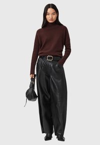 Burgunderfarvet strikket turtleneck sweater, sorte læderbukser med vidde, sort bælte med guldfarvet hardware, holder en lille sort taske.