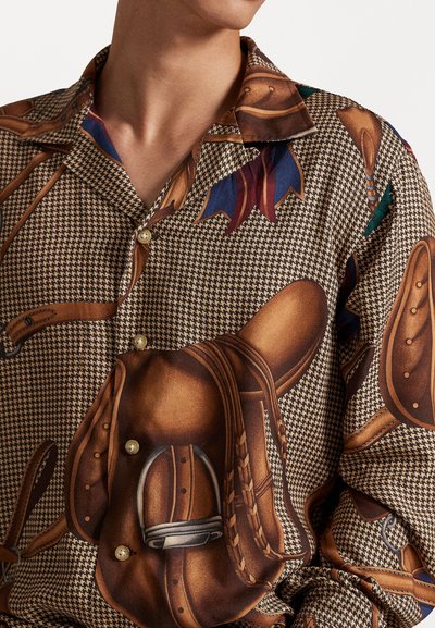 Camisa con patrón en marrón y beis de pata de gallo, que presenta ilustraciones de silla y correas. El material parece suave y cuenta con cierre de botones.