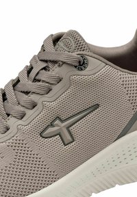 Ljust grå sportskor med ovandel i mesh, texturerad detaljering och mörkgrå accenter. Har rundad tå och vadderad vit sula.