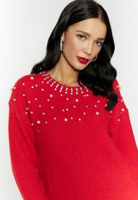 Maglione rosso lavorato a maglia con scollo rotondo decorato con paillettes e perle, texture morbida e stile leggermente oversize.