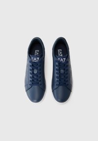 Navy blue sneakers with a smooth, synthetic upper, rounded toe, lace-up design, and white rubber outsole. Features a logo on the insole.