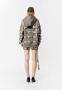 Sudadera con capucha en color topo con acentos de cinta metálica, que presenta un corte holgado y un diseño en capas. Combinada con una mini falda a juego y tacones negros.