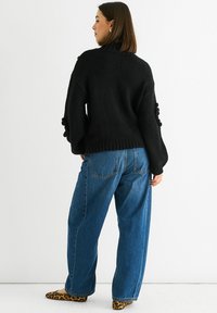 Black knitted sweater with puff sleeves, paired with high-waisted blue wide-leg jeans. Shoes feature a leopard print.